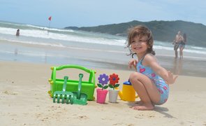 menina brincando com balde e plantas na praia